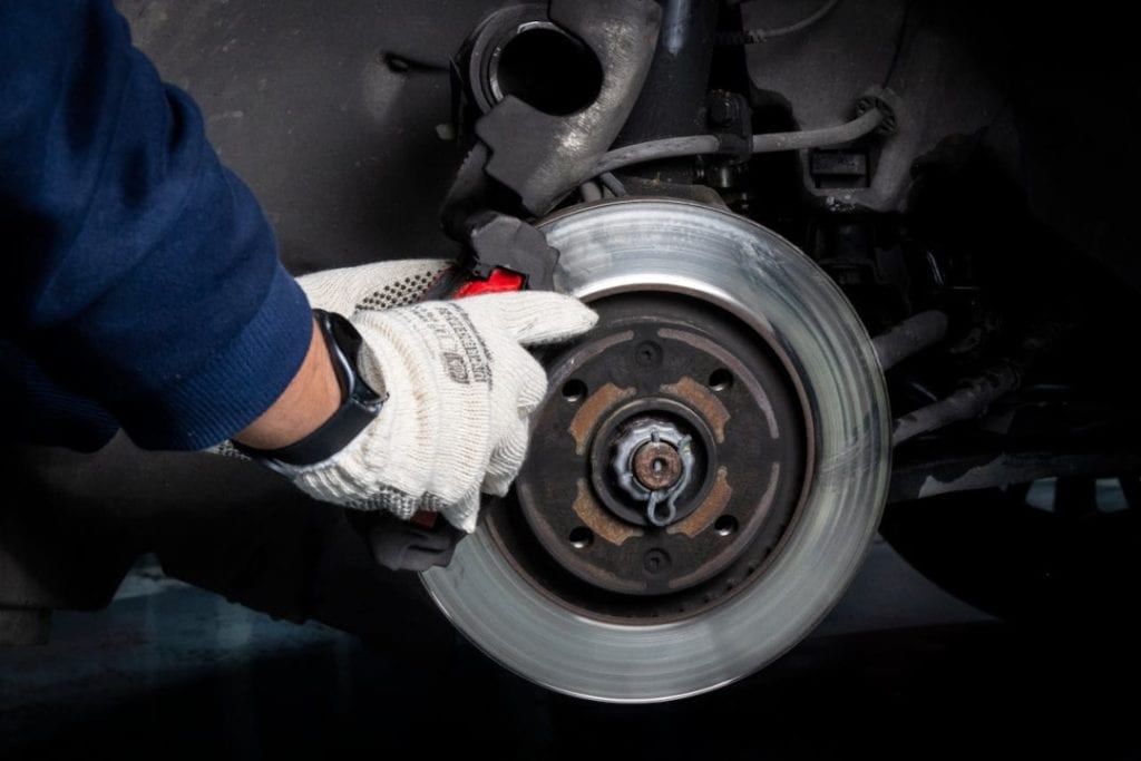 A gloved hand holding a brake disc on a car’s wheel hub.