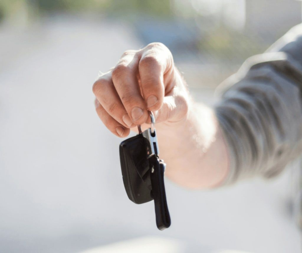 A hand holding out a car key to the next owner.