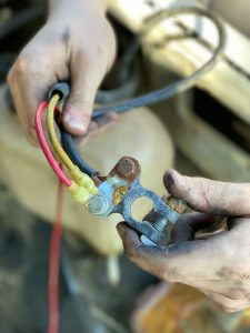 Hands holding a corroded battery terminal.