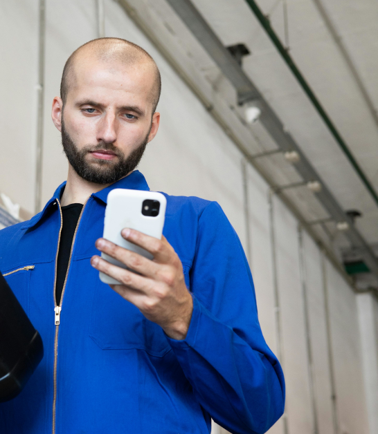 Mechanic in brightly-lit garage viewing a mobile phone.