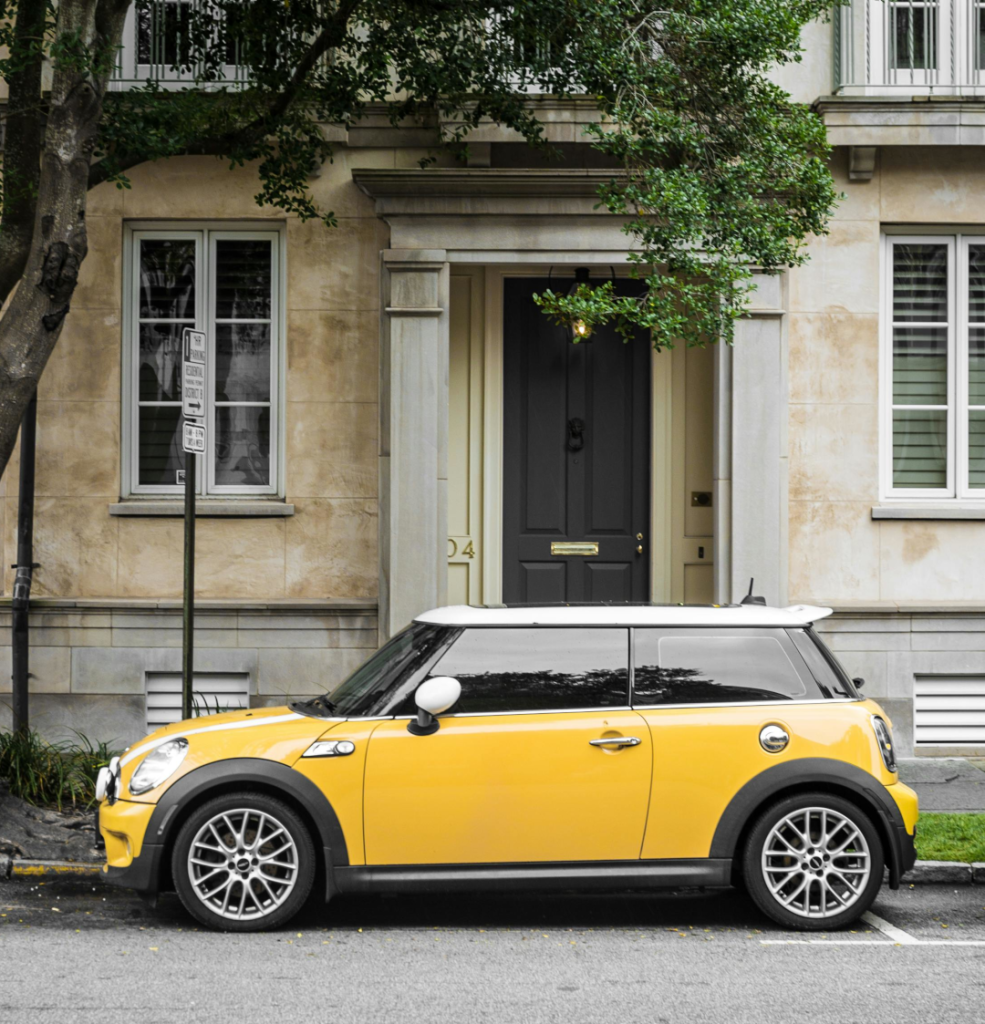 Yellow mini parked outside a rather posh looking residence.