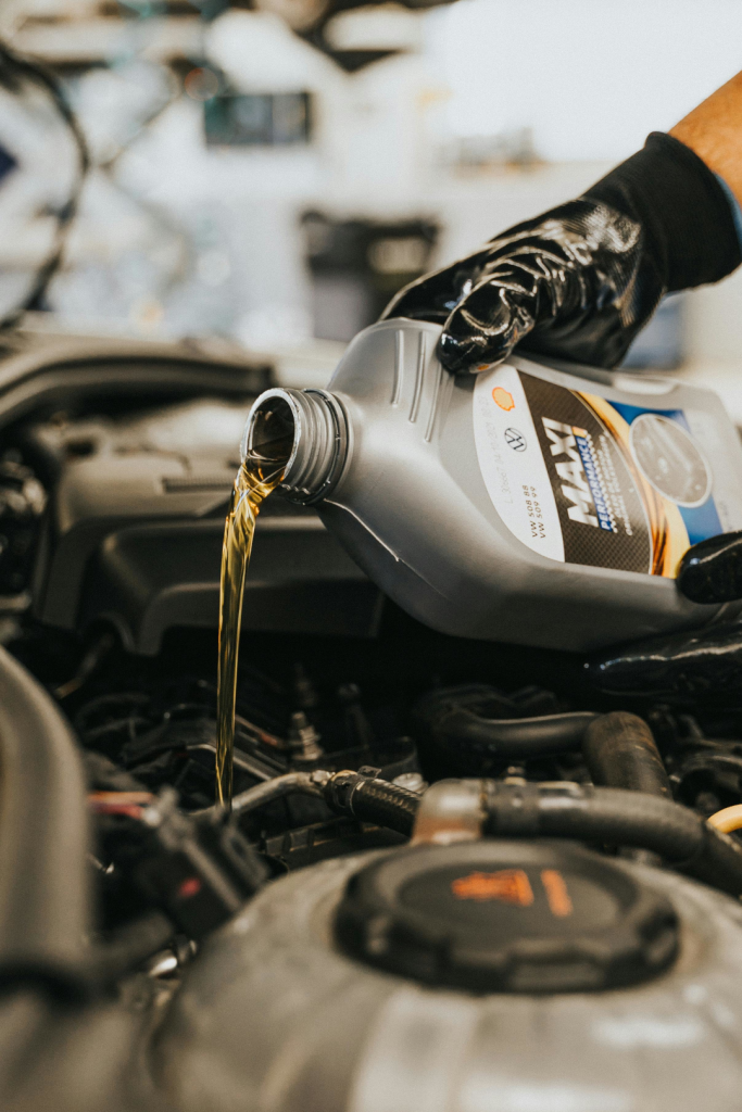 A hand pouring engine oil from oil bottle into oil tank.